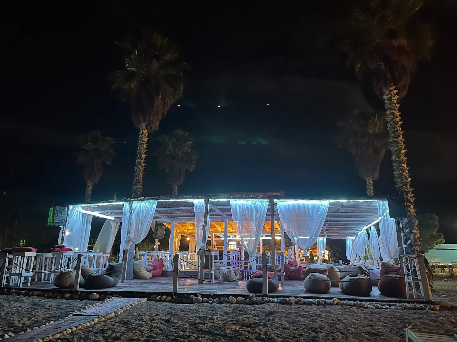 White-draped cabanas and beanbags lit with fairy lights on the sand at night at Friends Beach Bar, Jale