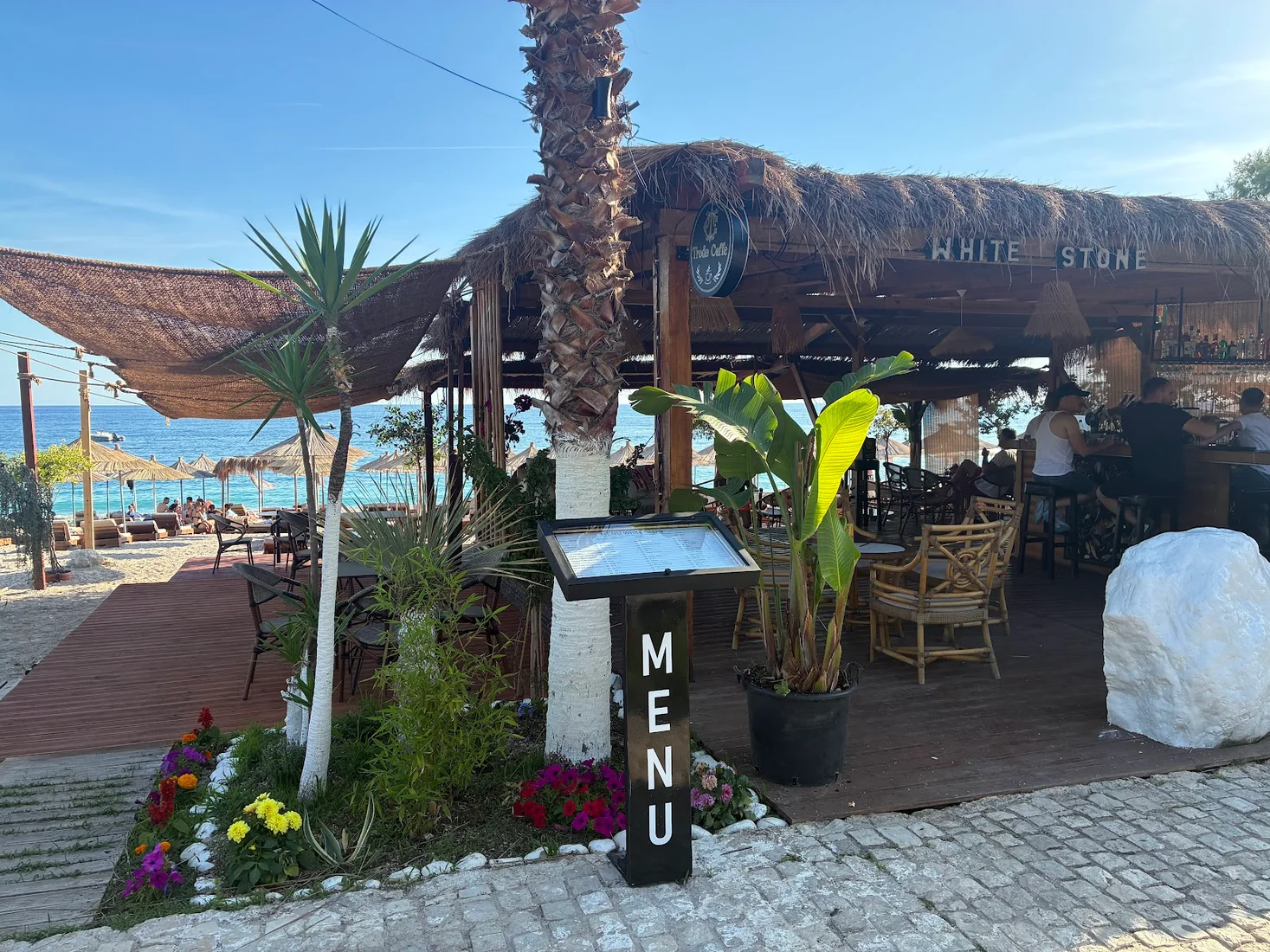 The thatched-roof White Stone beach bar with its menu stand and namesake white boulder on Dhërmi Beach