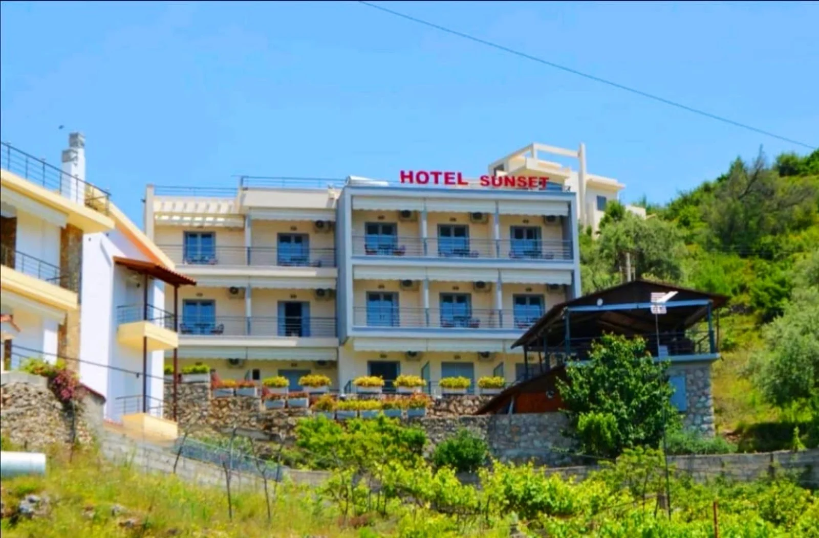 The pale facade of Hotel Sunset on the olive-terraced hillside at Dhërmi