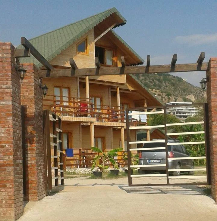 A timber chalet with a green roof behind a gated garden at Guesthouse Vila Druri in Dhërmi