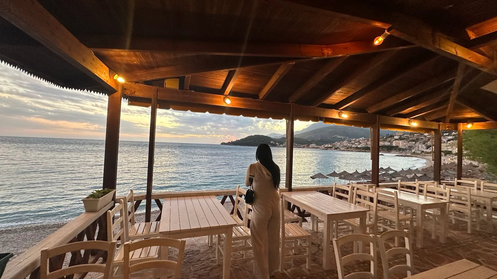 A wood-beamed beach terrace with white taverna chairs looking over the bay at dusk at Lui Potam, Potam beach near Himarë
