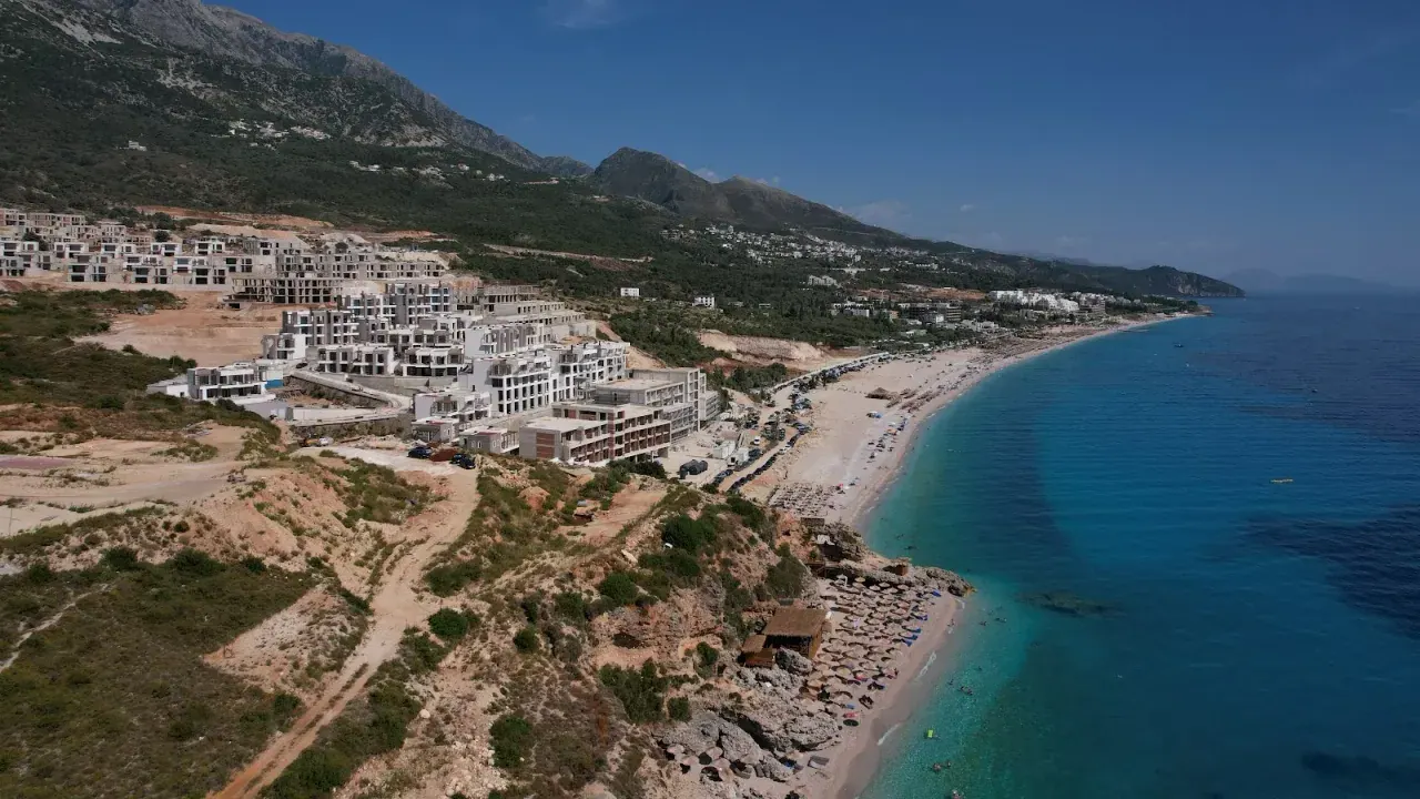Aerial view of Drymades Beach and its hillside resorts along the turquoise Ionian coast near Dhërmi