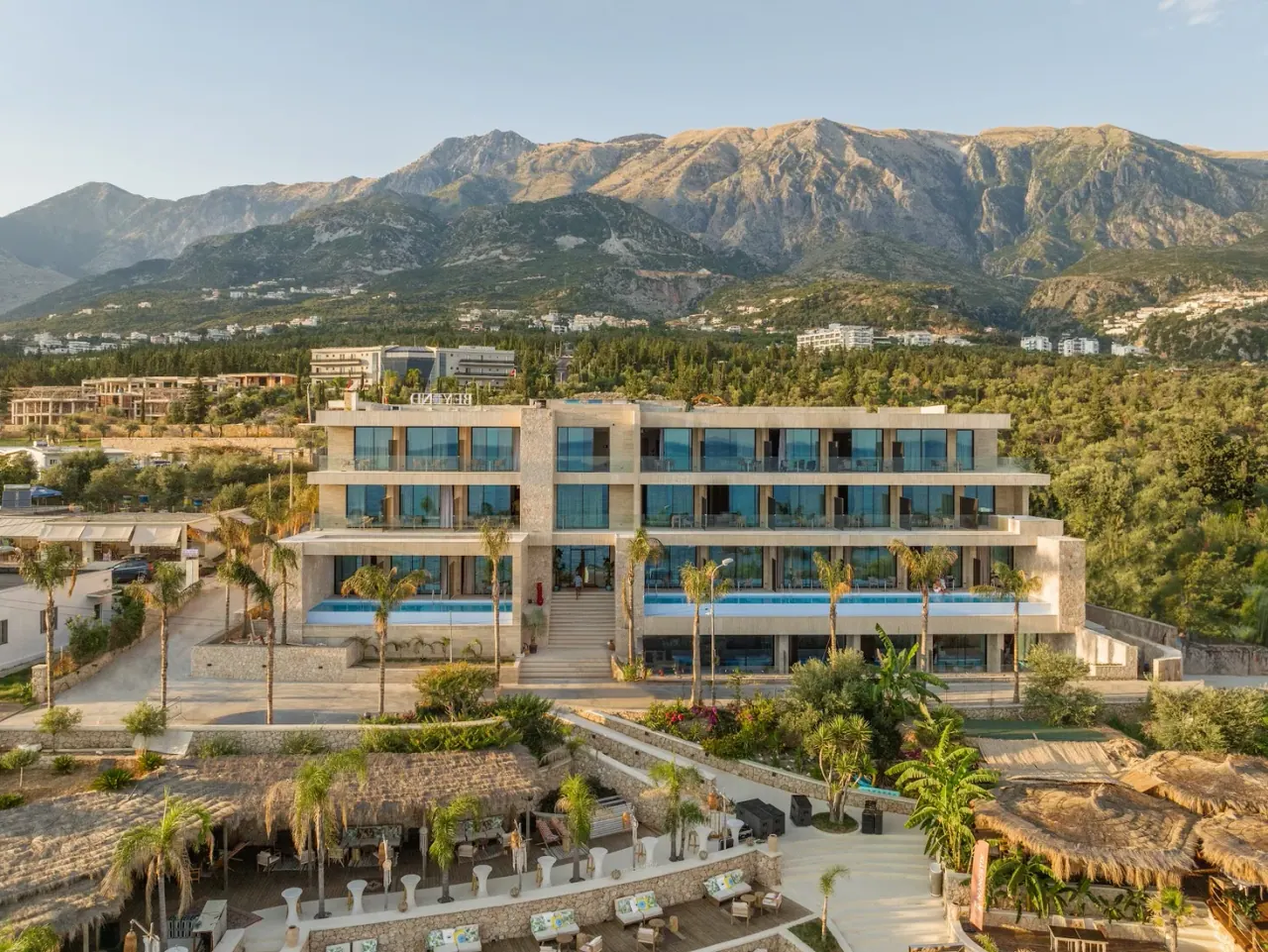The modern glass facade of BEYOND Boutique Hotel above its terrace pools on the Dhërmi shore