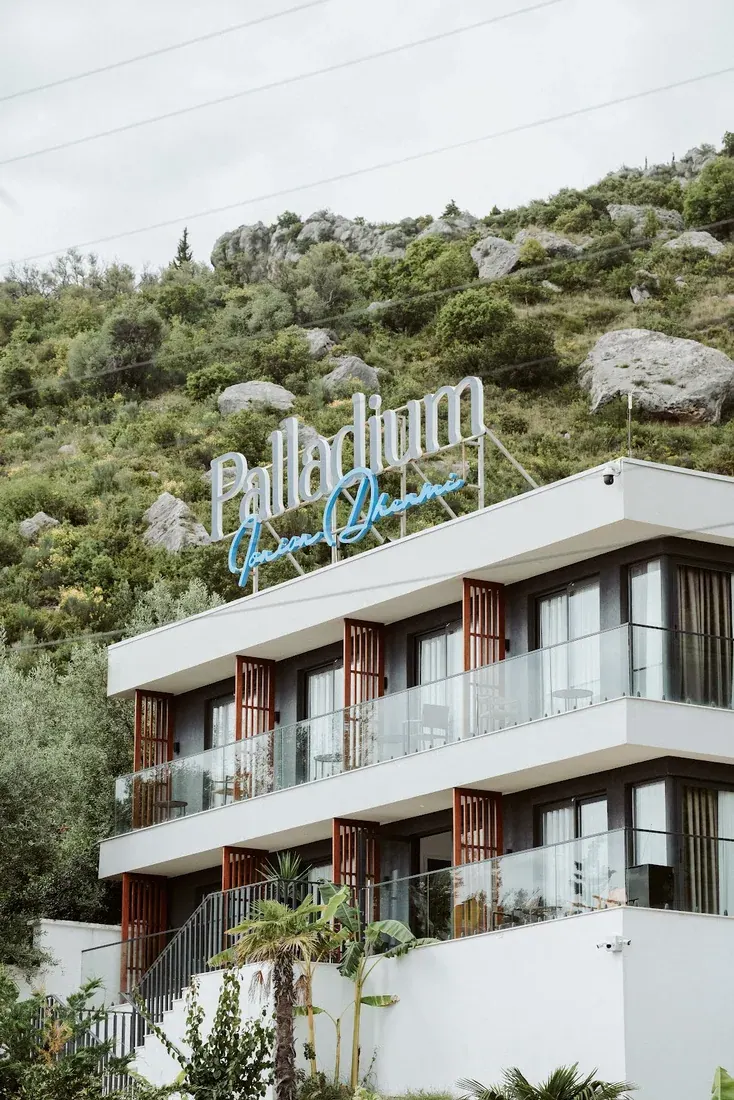 The white facade of Palladium Hotel with its rooftop sign against the hillside at Dhërmi beach