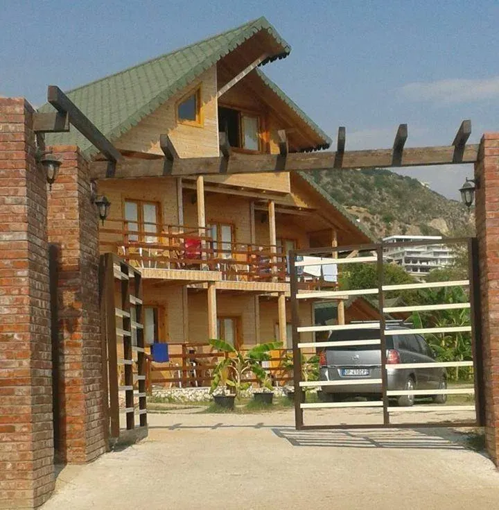 A timber chalet with a green roof behind a gated garden at Guesthouse Vila Druri in Dhërmi