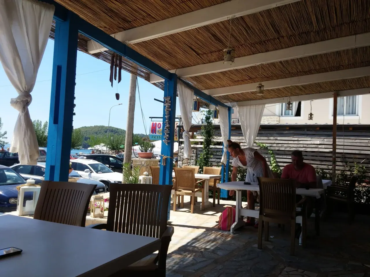 The thatched terrace and lit sign of Cibo Mare e Terra at dusk under woven rattan lamps in Himarë