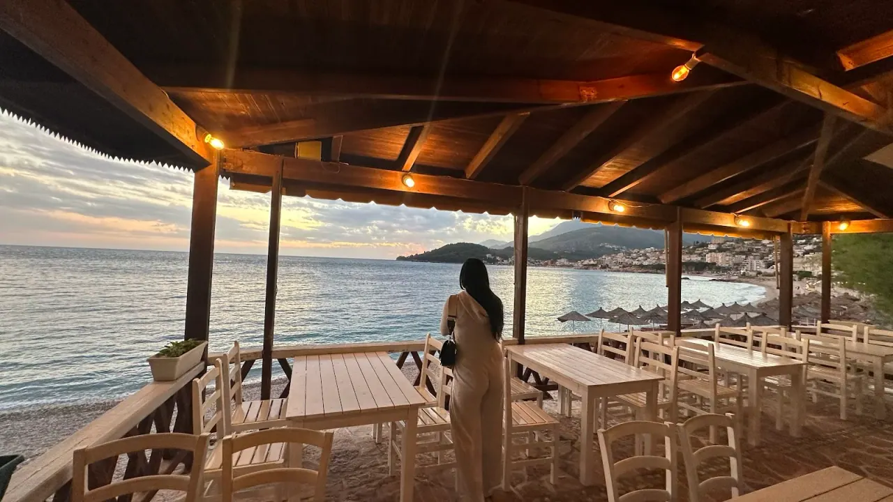 A wood-beamed beach terrace with white taverna chairs looking over the bay at dusk at Lui Potam, Potam beach near Himarë